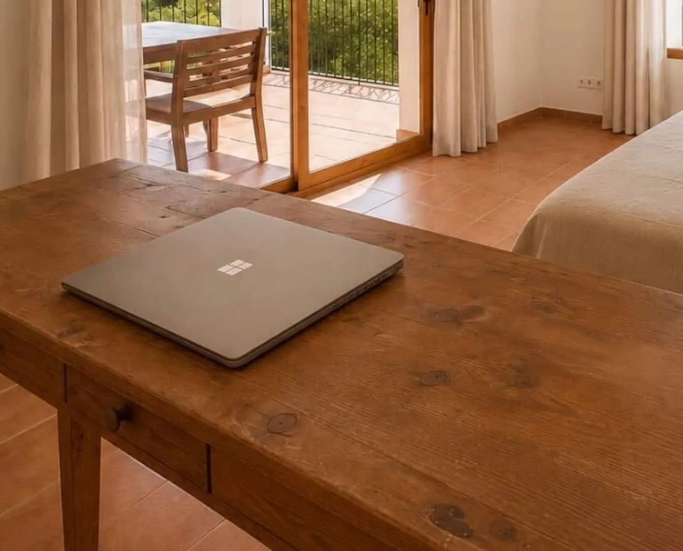 Mesa de madera con un ordenador portátil junto a la salida a un balcón con jardín